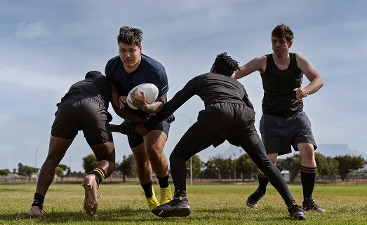 Des joueurs de rugby plaquant un adversaire lors d'un match sur un terrain en gazon, faisant preuve de force, d'esprit d'équipe et d'un esprit de compétition