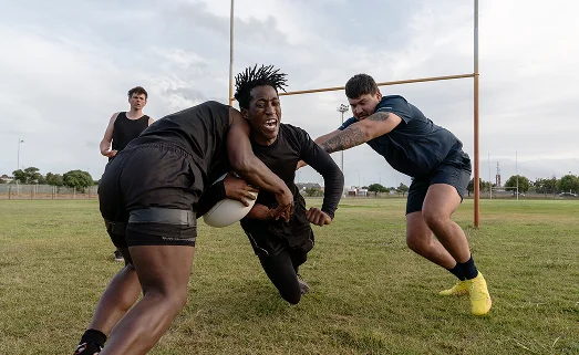 Des joueurs de rugby plaquant un adversaire lors d'un match sur un terrain en gazon, faisant preuve de force, d'esprit d'équipe et d'un esprit de compétition